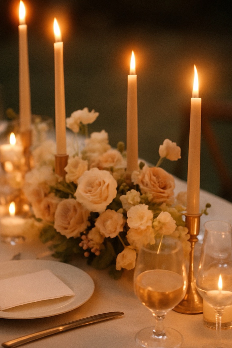 Mesa de recepção à luz de velas com flores em tons de blush e marcadores de lugar em papel de algodão